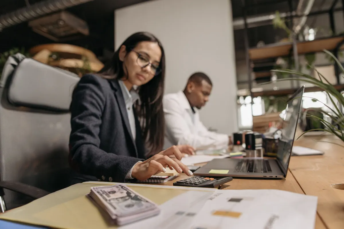 Two business professionals reviewing figures with a laptop and calculator at an office desk