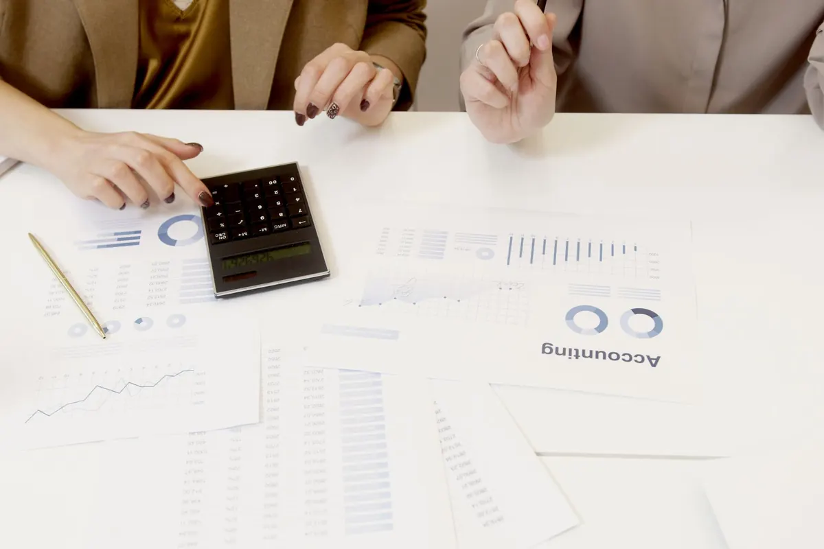 Two people reviewing printed financial reports and charts with a calculator