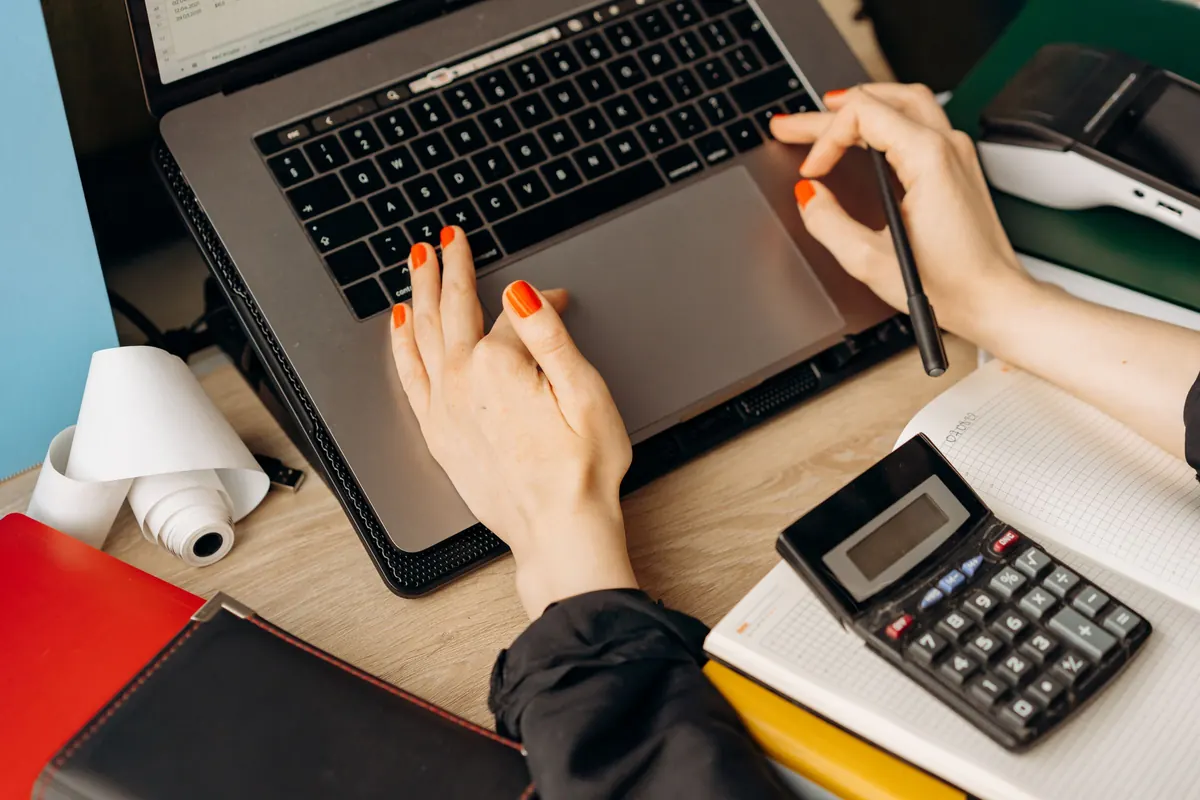 Hands entering figures on a laptop next to a calculator and receipts
