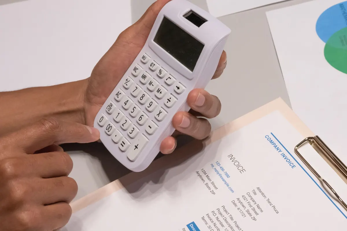 Hands using a calculator next to a printed invoice on a clipboard